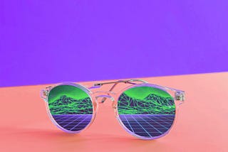 A pair of sunglasses reflecting a grid and a mountainous landscape sitting on a pink beach with a purple background.