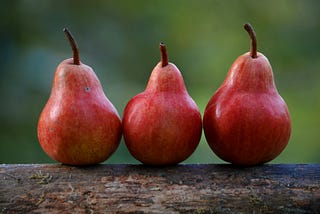 Three reddish pears sitting on a log