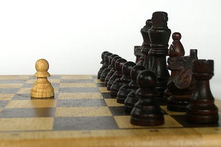 chess board with just one white pawn up against an entire fleet of black chess pieces, lined up.