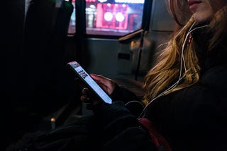 Girl with earbuds on looking at her phone while riding a bus