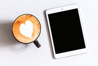 iPad on a white desk with a cup of coffee with a heart