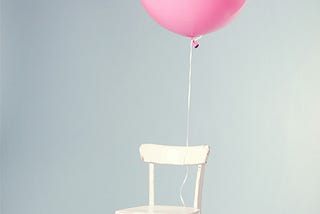 A single pink balloon, tied to a plain chair.