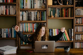 child sitting in front of laptop raising their arms in a gesture of success or sudden understanding