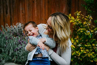 A woman with a young child. She is tickling him, he is laughing a lot and she is smiling.