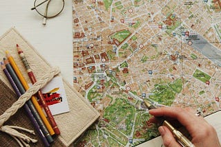 image of a map and notebook a man is writing on it, showing travel planning