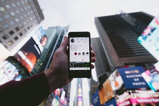 Hand holding phone featuring Instagram profile in front of Times Square in New York City.