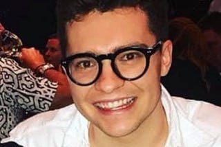 Photo of a smiling Jake Millar wearing his iconic thick-rimmed glasses