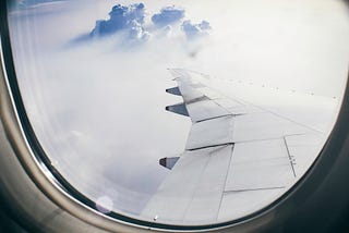 Looking out the airplane window, cumulus clouds and haze, all white, can be seen beyond the wing