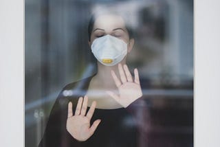 Photo of woman with face mask behind glass wall. Photo posted on Dr. James Goydos 2021 article about mask requirements and debate between Dr. Fauci and Rep. Jordan