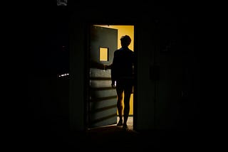 Man standing in a partially open, backlit doorway
