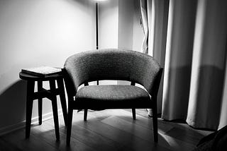 Black and white photo of an empty chair in the corner of a room