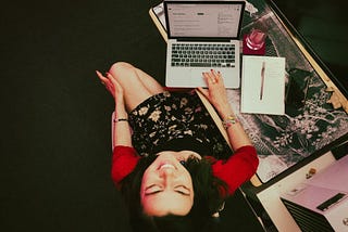 A young woman, the author, sits at a desk with a laptop and smiles.
