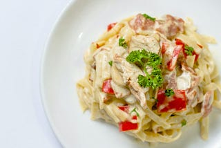 pasta in cream sauce with peppers and parsley topping on white plate