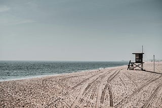 An isolated life guard tower situated on a sandy beach facing the Pacific Ocean.