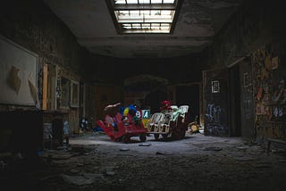 A dark abandoned room, strewn with garbage with graffiti on the walls. In the middle of the room sits a variety of toys that will never make it to the store shelves.