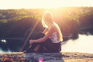 beautiful blond gazes at a river below a mountain with sunset in background