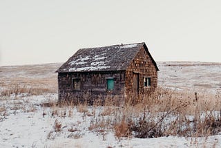 A lonely cabin sits alone on a snowy, icy and barren landscape.