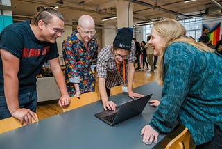 Four Makers students standing around a laptop talking and smiling