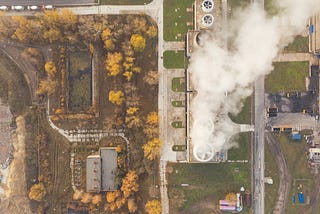 A bird’s eye view of a large factory area with white smoke coming out of the chimneys.