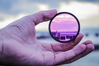 A UV-like lens being held by a left hand’s thumb and forefinger.