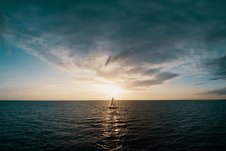 A sailboat in the ocean at the sunset.