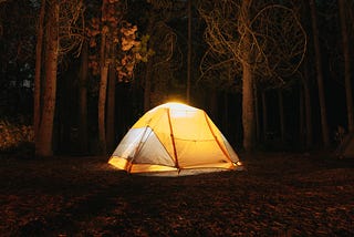 A glowing yellow camp tent in a forest at night