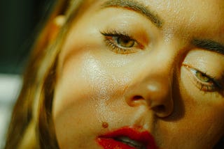 A close up of a woman’s face who looks sweaty and lathargic.