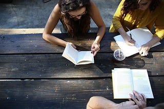Three people sit around a table, reading.