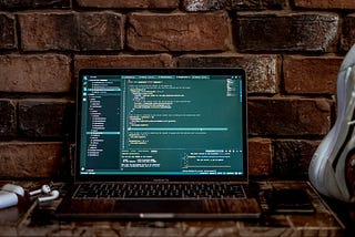 Laptop featuring code. To the right, a person has their feet kicked up on the table.