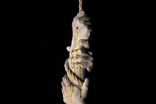 Hands pulling a rope with gold paint dripping on the hands.