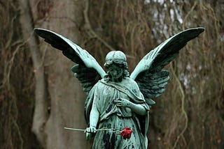 An old worn statue of a solemn angel holding a red rose.