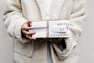 A girl holding three white blocks stacked one on top of each other, with each have a written word on it, spelling: “Spirit of Adoption”.