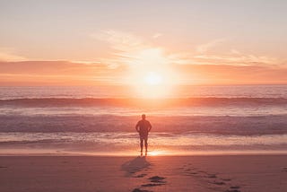 A calm person stands on the beach looking out to sea