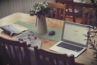 wood dining room table with open laptop and newspaper on it.