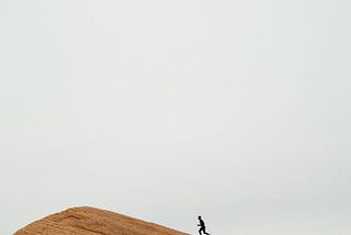Runner in the distance nearing top of a red stone hill.