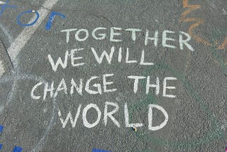 A photo of a sidewalk, with the words “together we will change the world” written in chalk
