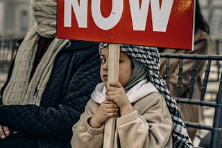 Palestinian child holding a sign saying ceasefire now.