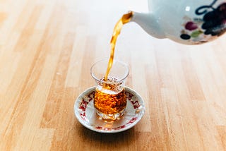 A cup of black tea, being poured from a teapot.