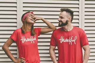 a happy couple wearing matching red shirts that say ‘thankful’