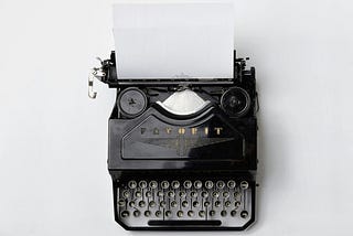 A black typewriter with a page and indescernable words on it.