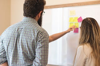 a group of 3 young professionals looking at a white board with sticky notes