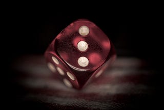 A red die being rolled and showing three dots in front of a black background