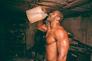 topless muscled man drinking water from a jug in a gloomy room