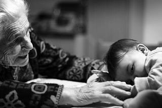 An elderly woman reaches out to a sleepy baby.