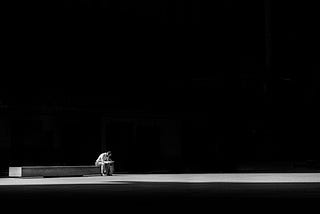 A man sitting on a bench in middle of darkness.