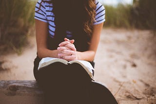 Girl with hands clasped praying with Bible on her lap.