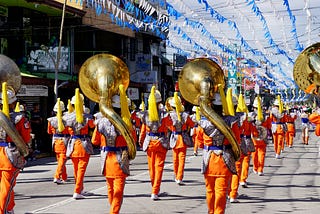 A marching band wearing orange outfits, carrying lots of tubas.