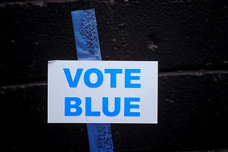 A sign taped on a brick wall that reads “vote blue.”