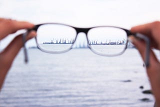 A pair of glasses in the foreground focus to reveal machinery in the ocean in the background