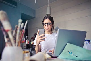 Woman looking at mobile phone next to a laptop